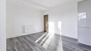 Een ruime kamer met een houten vloer, witte wanden en een radiator.