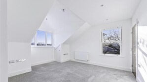 Een ruime zolderkamer met een schuine kap, grote ramen en een radiator.