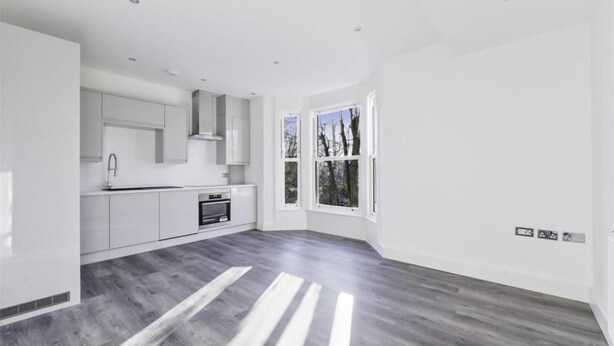 Een moderne keuken met witte kastjes, een inbouwoven en een raam met uitzicht op bomen.