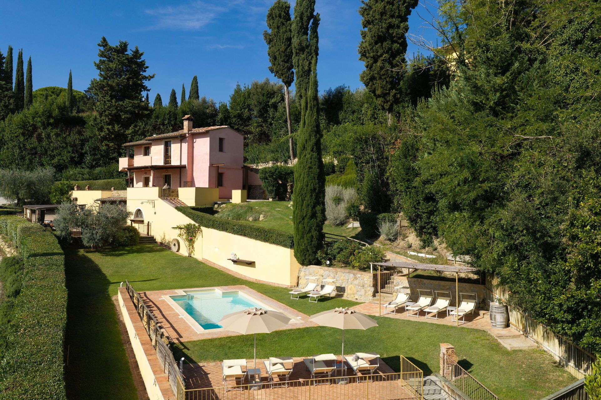 A two-story building with a swimming pool, sun loungers, and a stone wall.