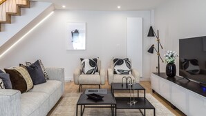 A modern living room with a staircase, a sofa set, two armchairs, a coffee table, a TV, and a floor lamp. - Modern Family Home in Kensington (London)