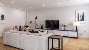 A modern living room with a grey sofa, a flat-screen TV, and a small side table. - Modern Family Home in Kensington (London)