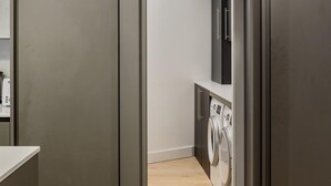A modern laundry room with a washing machine and dryer, wooden flooring, and a minimalist design. - Modern Family Home in Kensington (London)