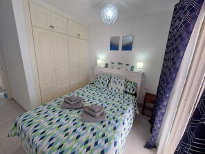Une chambre à coucher comprenant un lit, une armoire, deux œuvres d’art murales et un luminaire suspendu.