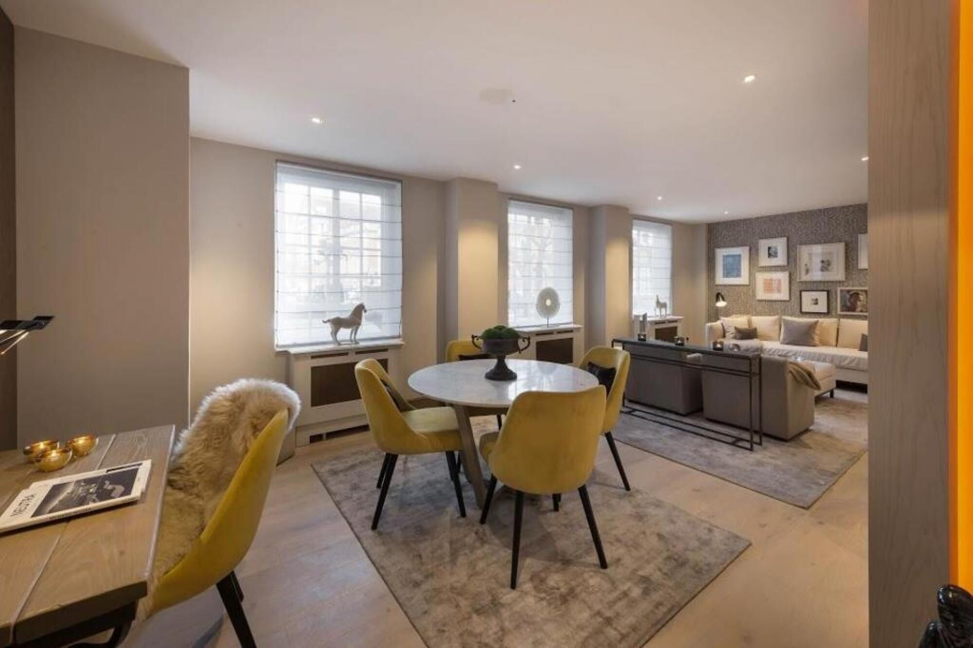 A modern living room with a round dining table, yellow chairs, a sofa, and a kitchen area.