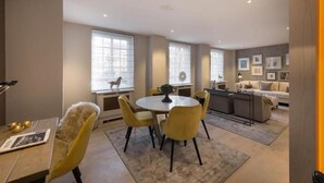 A modern living room with a round dining table, yellow chairs, a sofa, and a kitchen area. - 4-bedroom Apartment in the Heart of Chelsea (London)