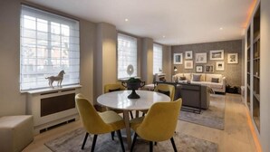 A modern living room with a round dining table, yellow chairs, a sofa, and a kitchen area. - 4-bedroom Apartment in the Heart of Chelsea (London)