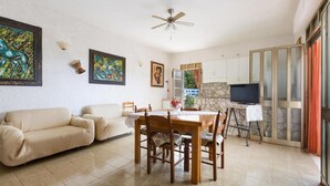 Un soggiorno con un divano, un tavolo da pranzo con sedie, una ventola a soffitto e opere d'arte alle pareti.