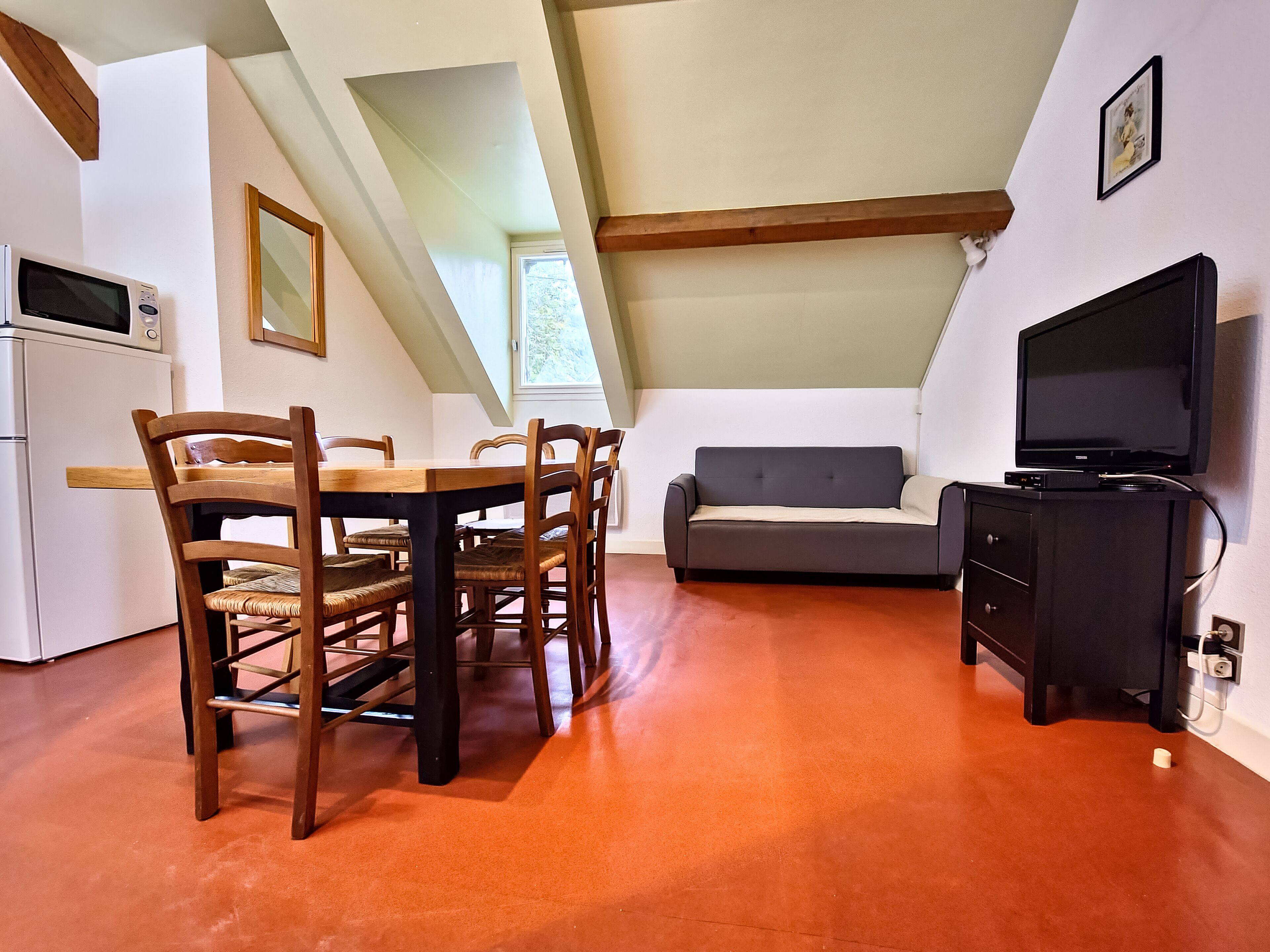 Una habitación acogedora en el desván con una mesa de comedor, sillas, un sofá y un televisor.