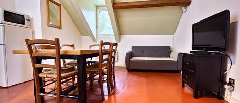 Una habitación acogedora en el desván con una mesa de comedor, sillas, un sofá y un televisor.