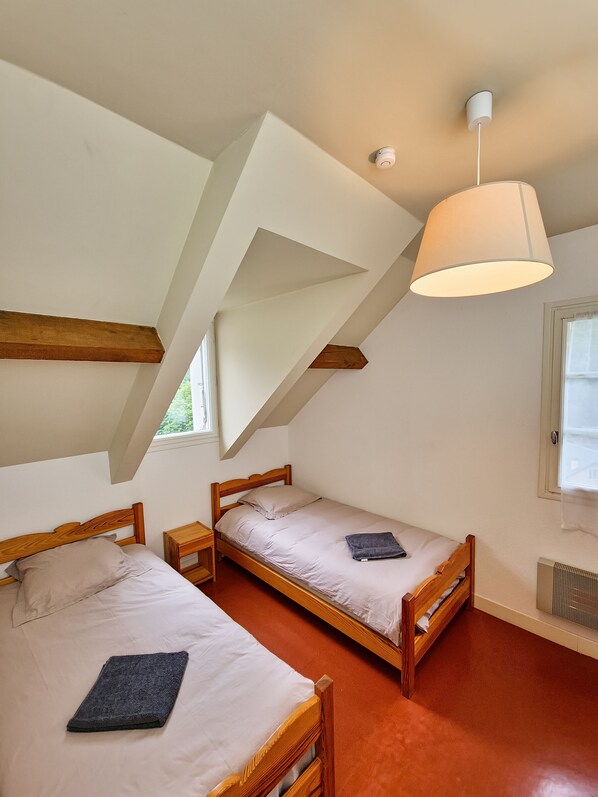 Ein Schlafzimmer mit zwei Holzbetten, einer geneigten Decke und einem Fenster.
