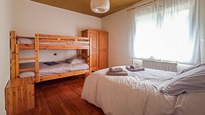 Un dormitorio con literas, un armario, un radiador y una ventana con cortinas.