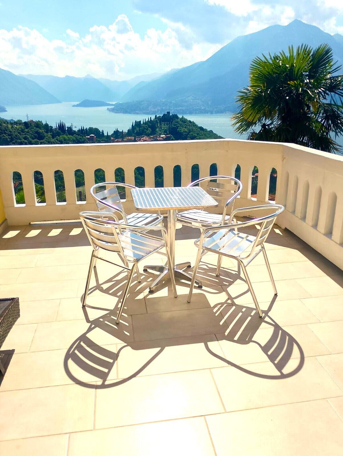 Une terrasse avec une table et des chaises, offrant une vue sur un paysage montagneux et une étendue d’eau.