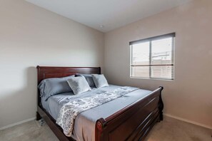 A bedroom with a wooden bed, a window with blinds, and a carpeted floor.