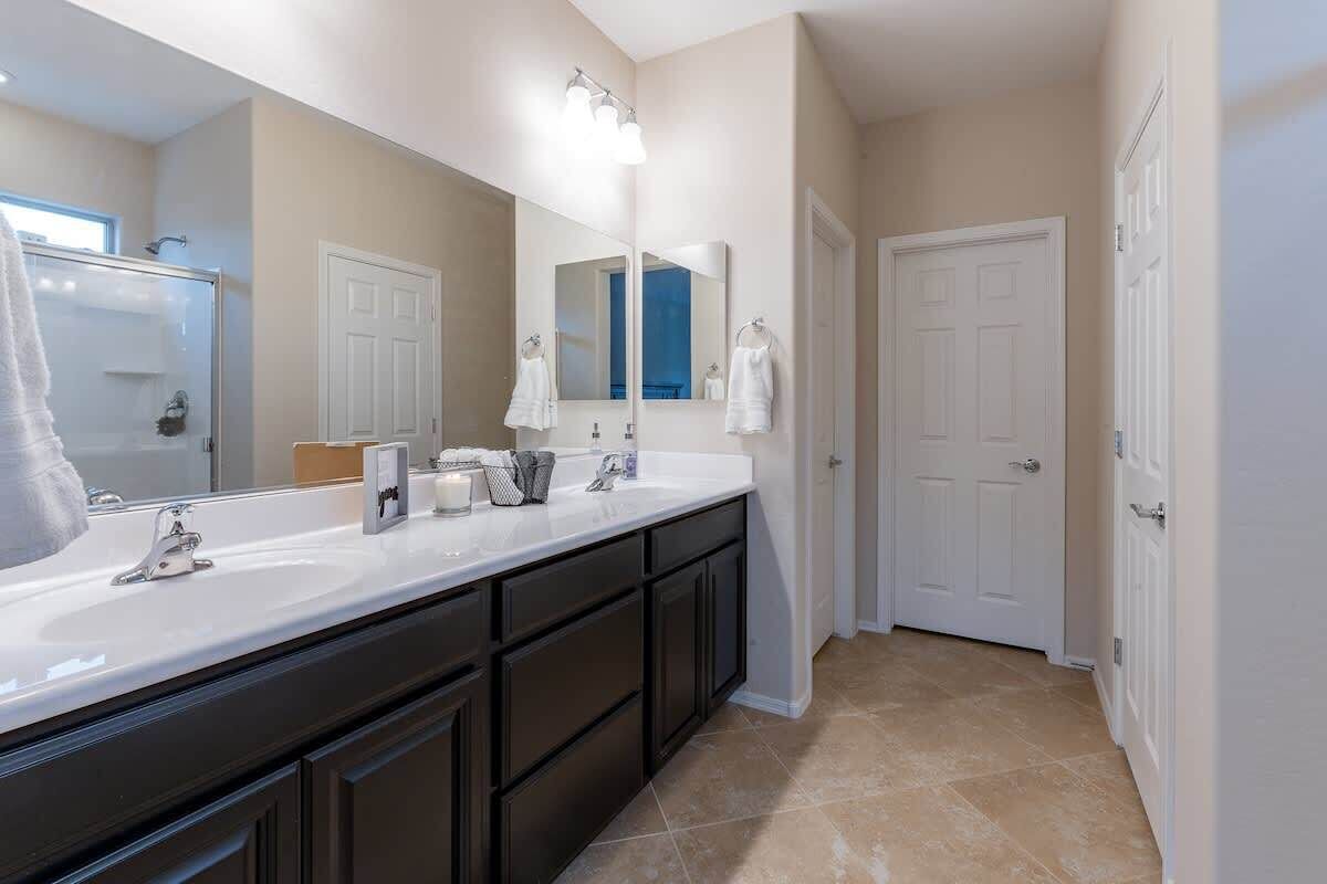 A bathroom with a double sink vanity, a large mirror, and a shower area.