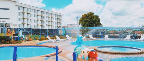 A hotel with multiple swimming pools, lounge chairs, and a large building in the background.