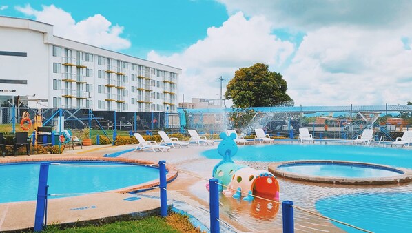 A hotel with multiple swimming pools, lounge chairs, and a large building in the background.