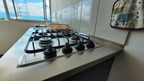 A kitchen with a gas stove, a window with a view of the sky, and a wall-mounted coffee-themed cloth. - Apartment 5 minutes from the Coffee Park, near Panaca, Salento, Cocora. (Montenegro)