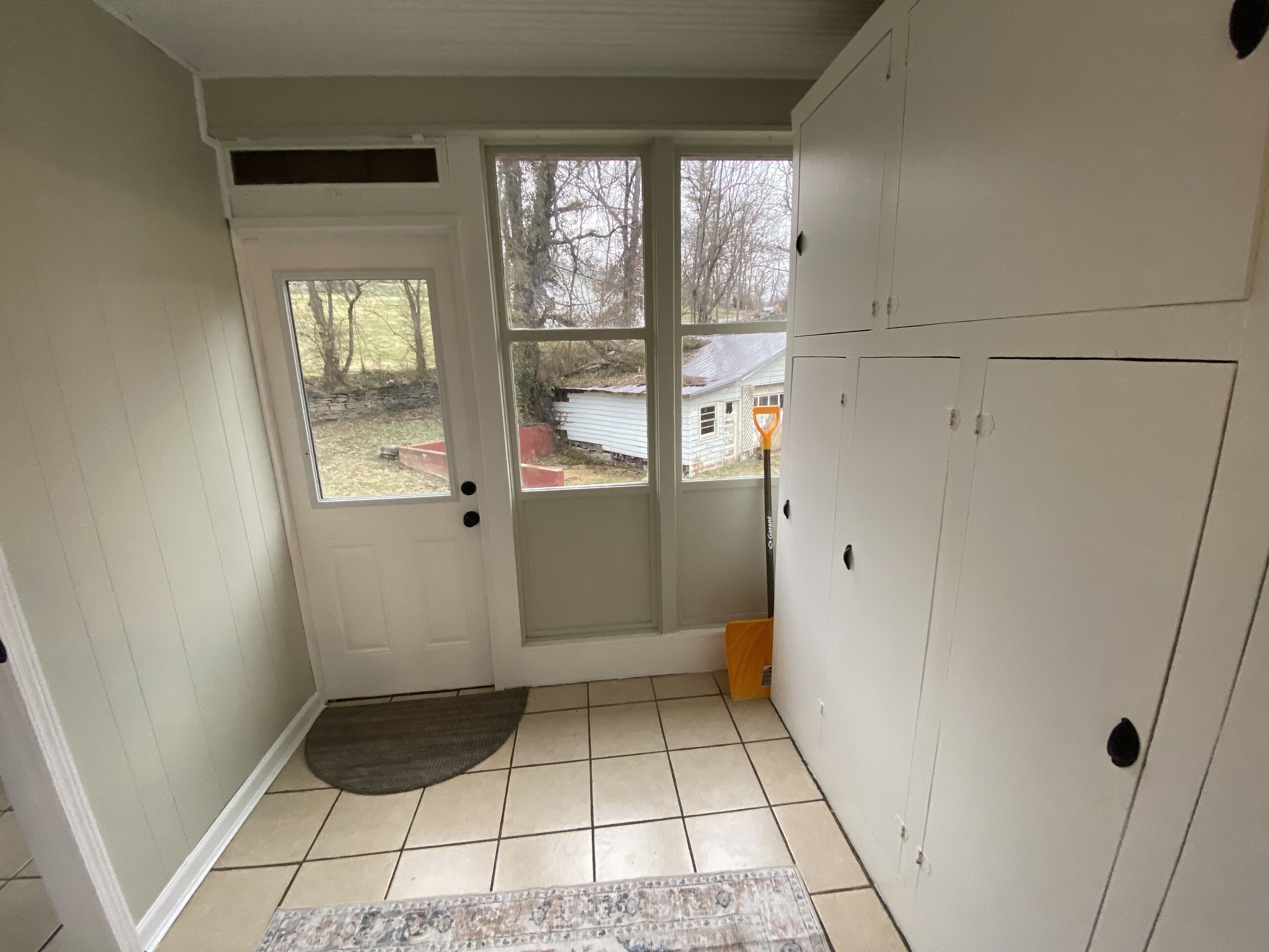 A room with a white door, a small rug, and a view of a house through the door.