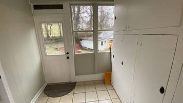 A room with a white door, a small rug, and a view of a house through the door.