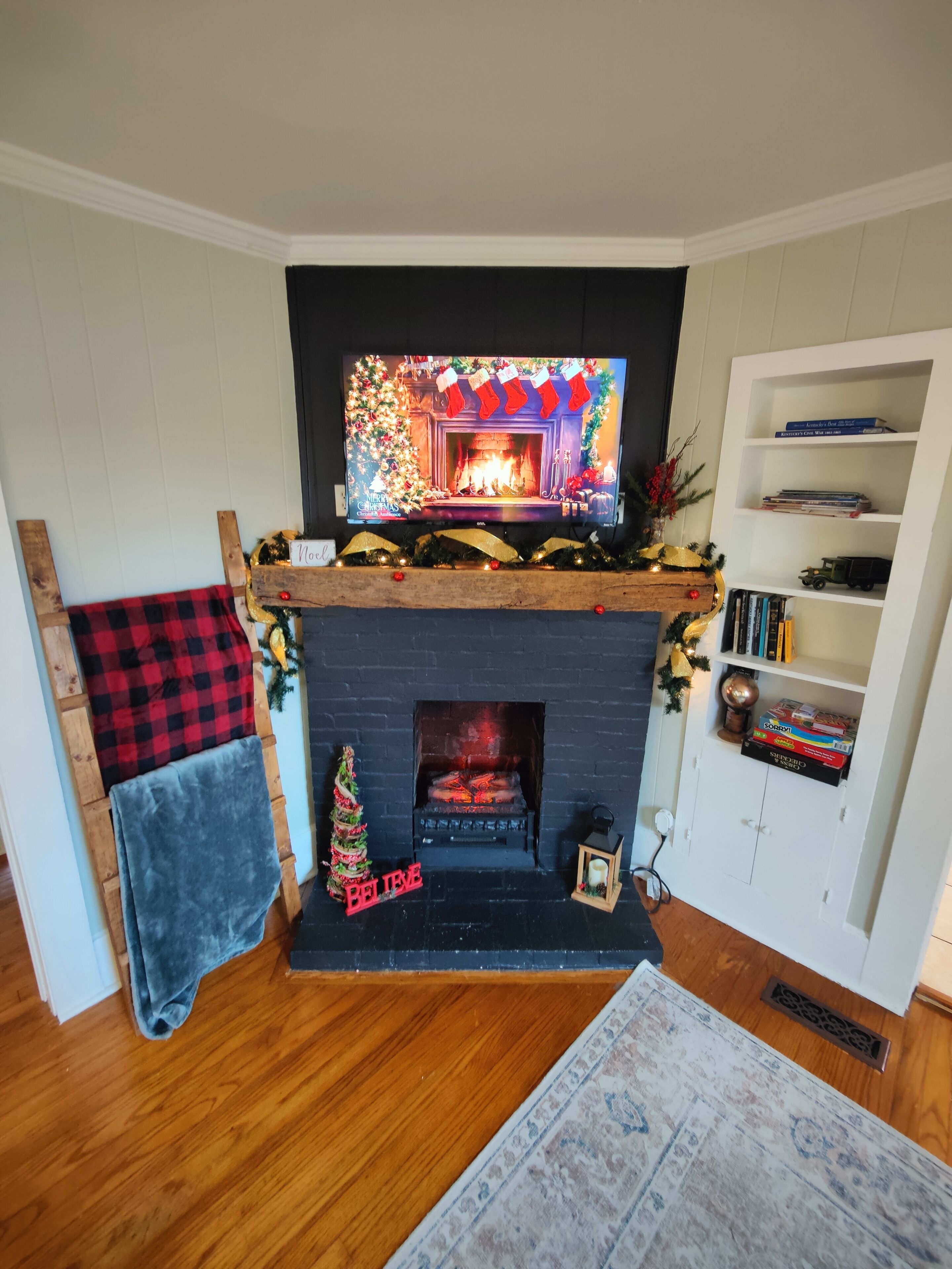 A living room with a fireplace, a television mounted above it, and a bookshelf to the right.