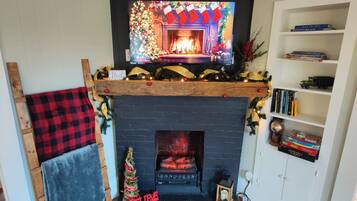A living room with a fireplace, a television mounted above it, and a bookshelf to the right.