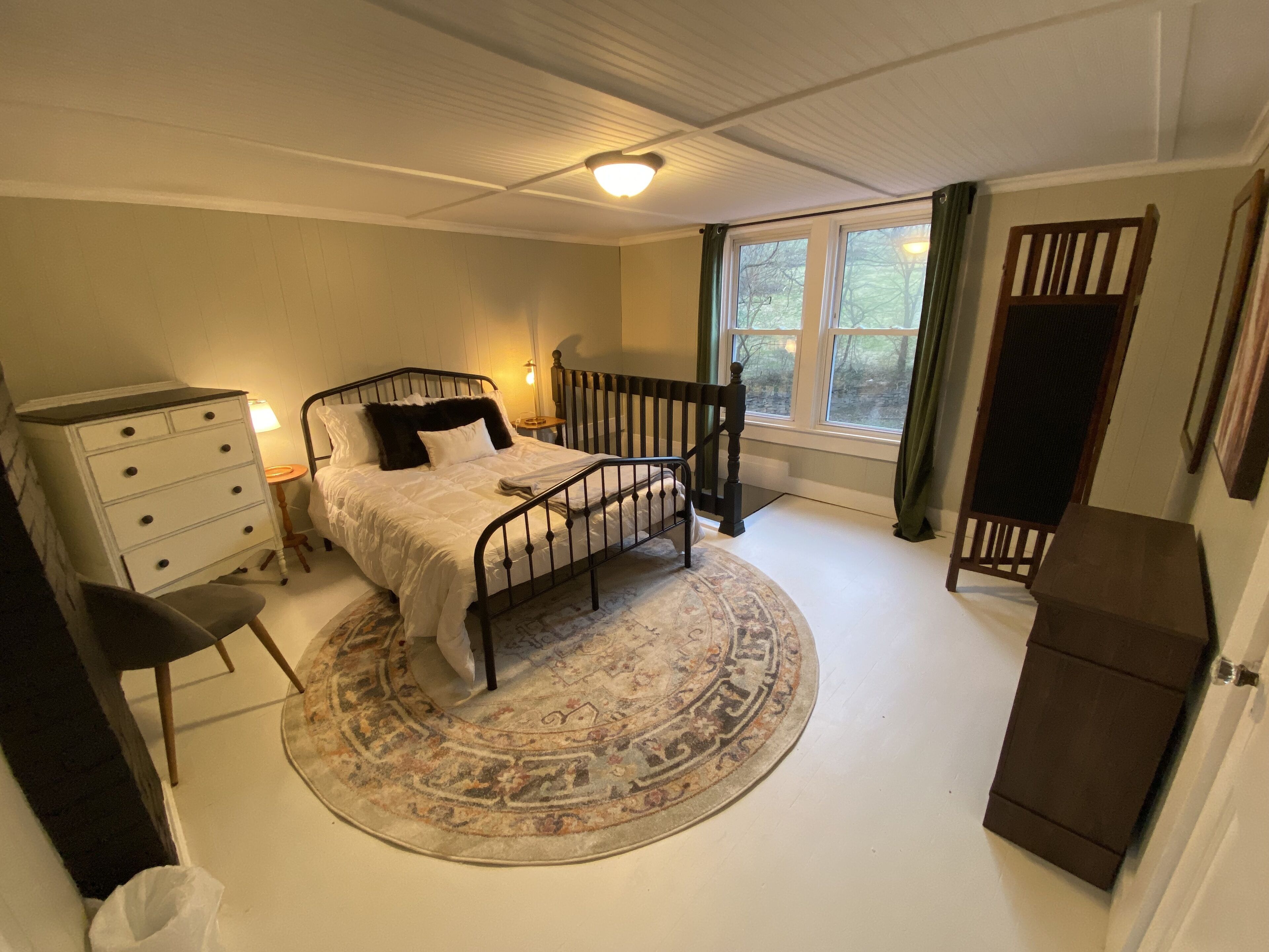 Une chambre à coucher avec un lit, une commode, une chaise et une fenêtre avec des rideaux.