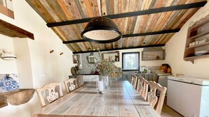 A rustic dining area with a wooden table and chairs, a hanging light fixture, and a kitchen in the background. - MAS GINJOL (Tortosa)