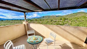 A covered outdoor area with a table and chairs, a view of green hills and wind turbines in the distance. - MAS GINJOL (Tortosa)