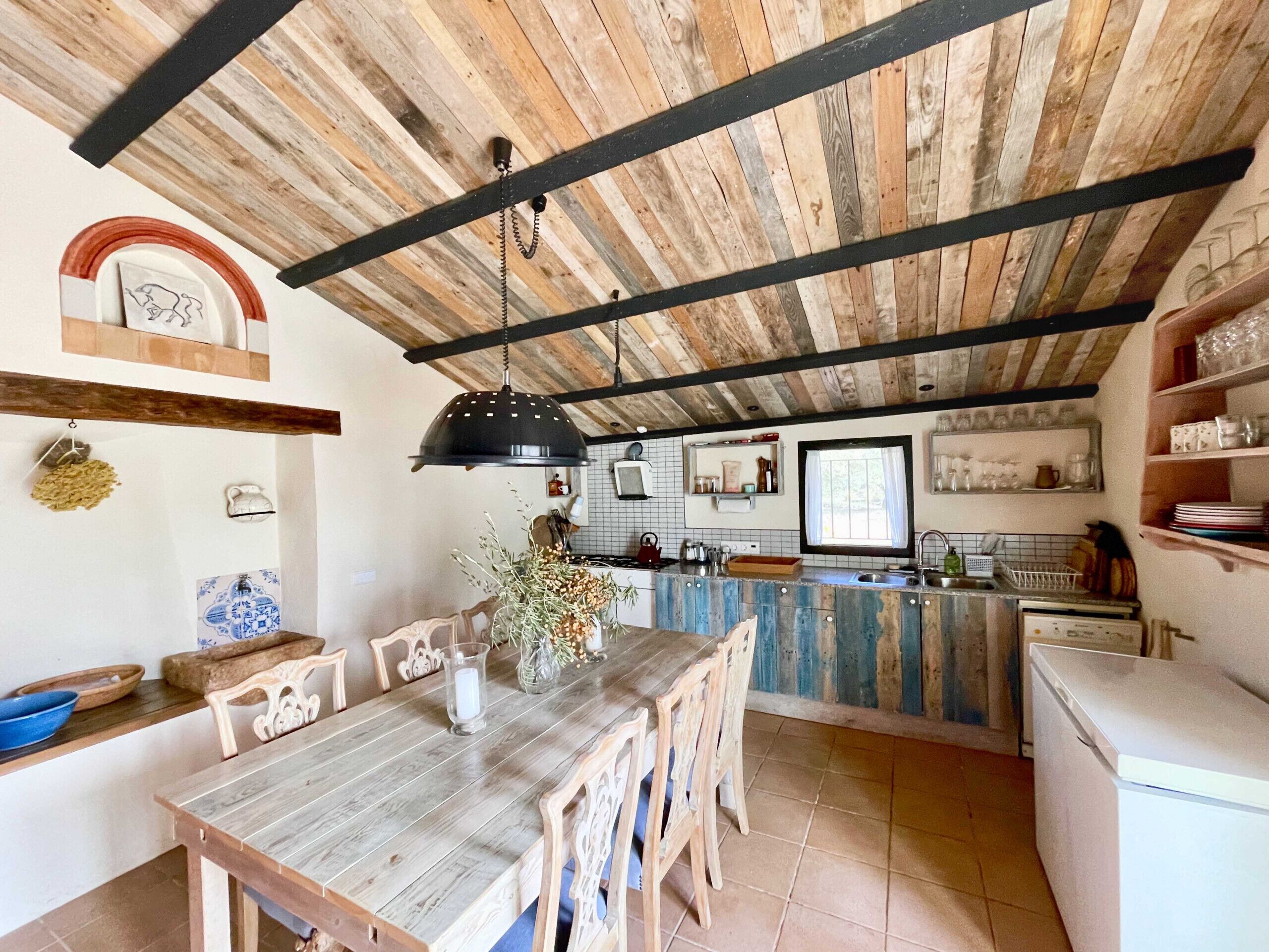 A rustic kitchen with wooden beams, a dining table with chairs, and a kitchen island.