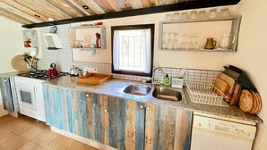 A kitchen with a rustic wooden ceiling, a built-in stove, a sink, and a window with curtains. - MAS GINJOL (Tortosa)