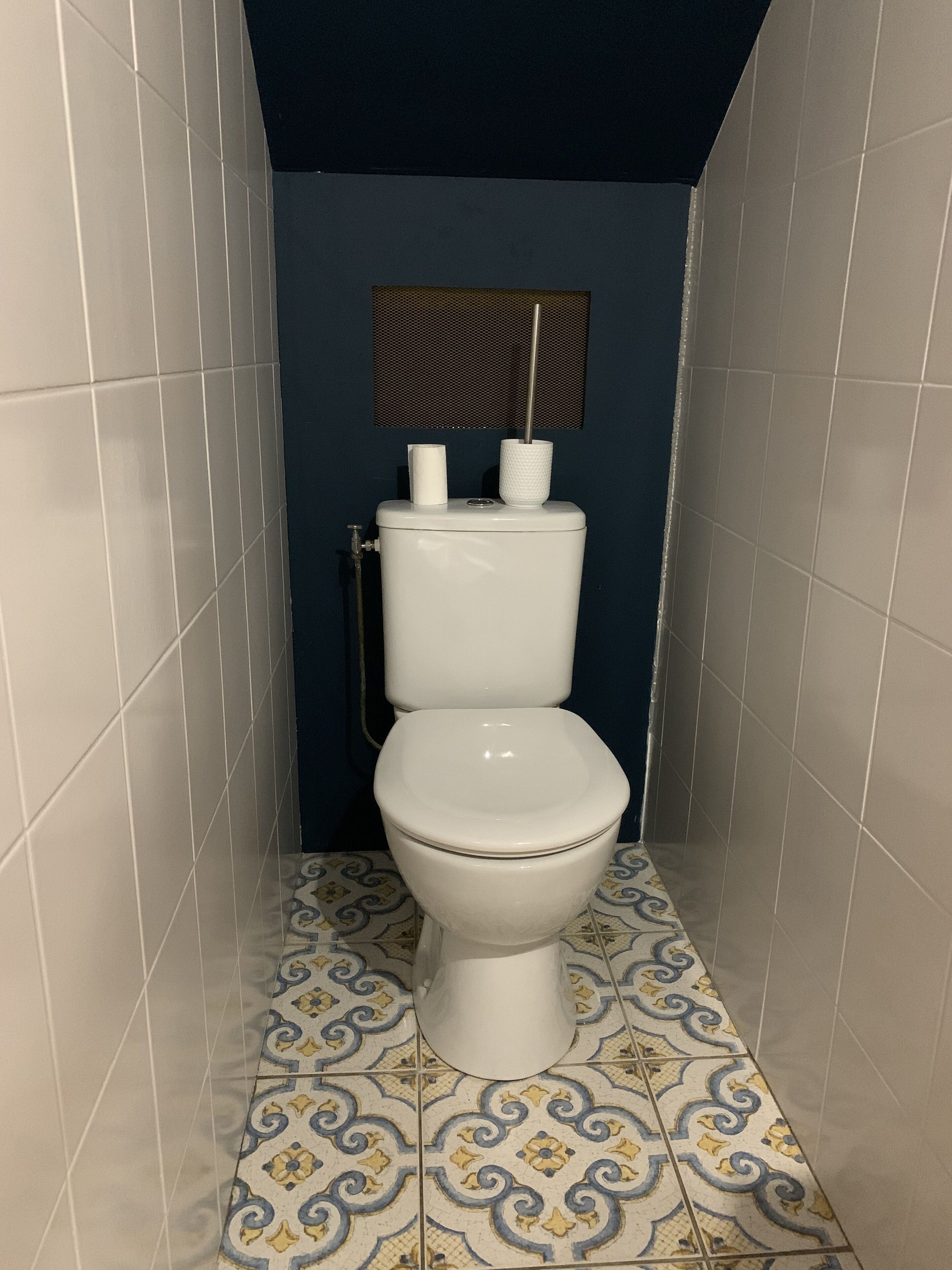 A bathroom with a toilet, a toilet paper holder, and a wall-mounted vent.