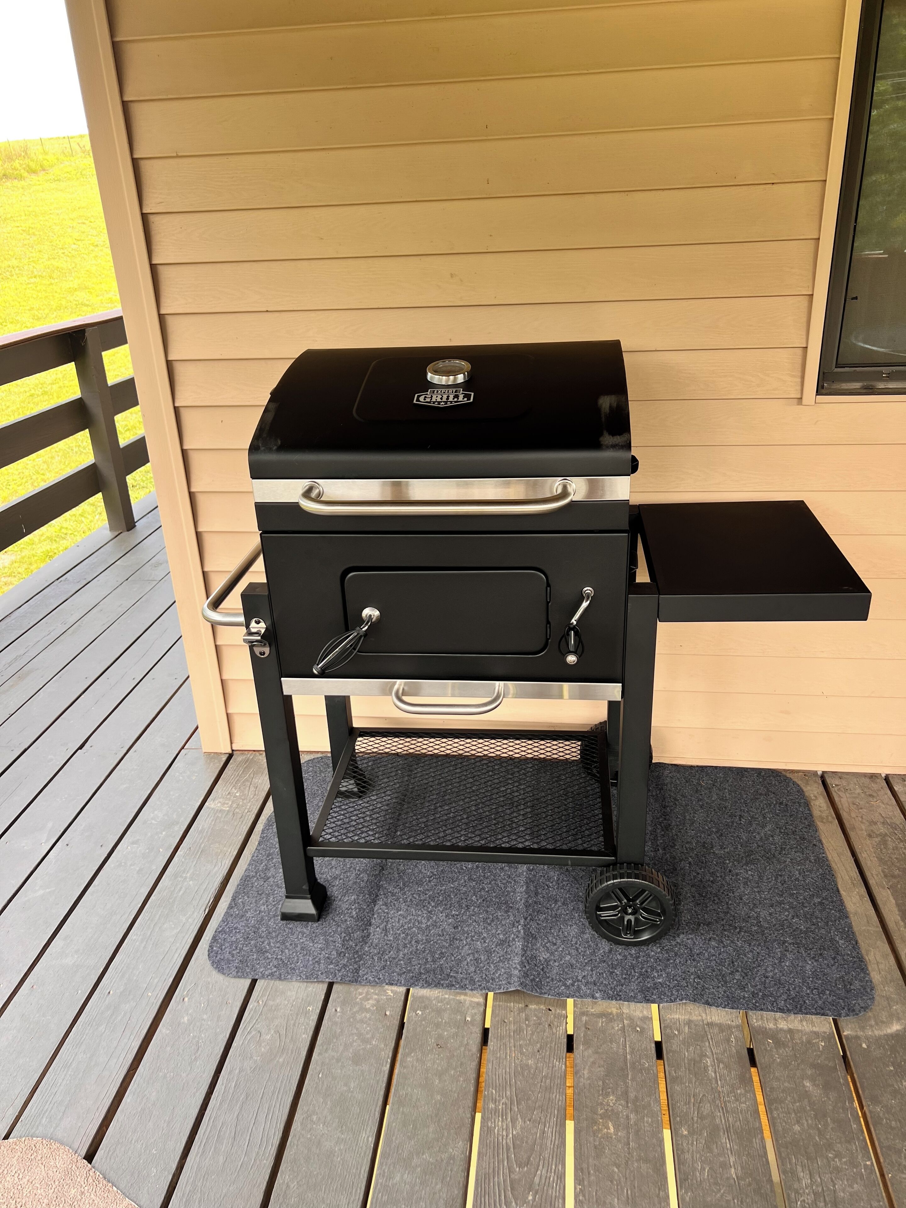 A portable grill on a wooden deck with a metal grate underneath.