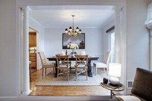 A dining area with a wooden table, chairs, a chandelier, and a framed picture above the table.