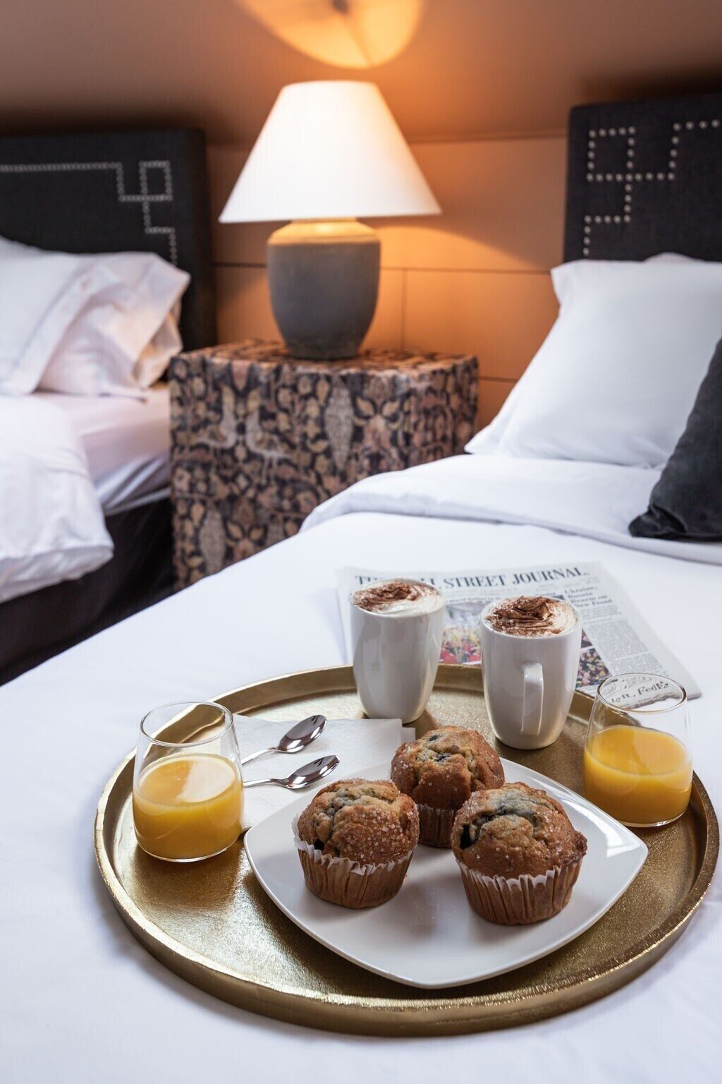 A neatly made breakfast tray with muffins, coffee, and orange juice on a bed in a hotel room.