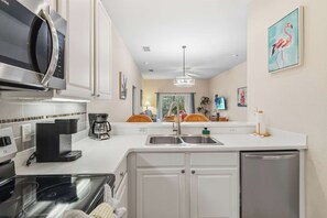 A modern kitchen with a microwave, coffee maker, and dishwasher. There is a large window with a view of the outdoors.