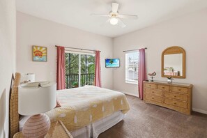 A bedroom with a bed, a dresser, a ceiling fan, a television, and a window with curtains.