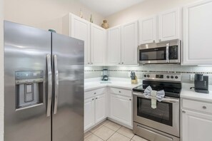 Una cocina moderna con armarios blancos, electrodomésticos de acero inoxidable, incluyendo refrigerador, microondas y horno, y un backsplash de azulejos.