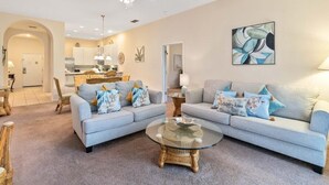 A living room with two sofas, a glass coffee table, wicker chairs, a ceiling fan, and a kitchen in the background. - Bahama Bay third floor unit close to Disney (Davenport)
