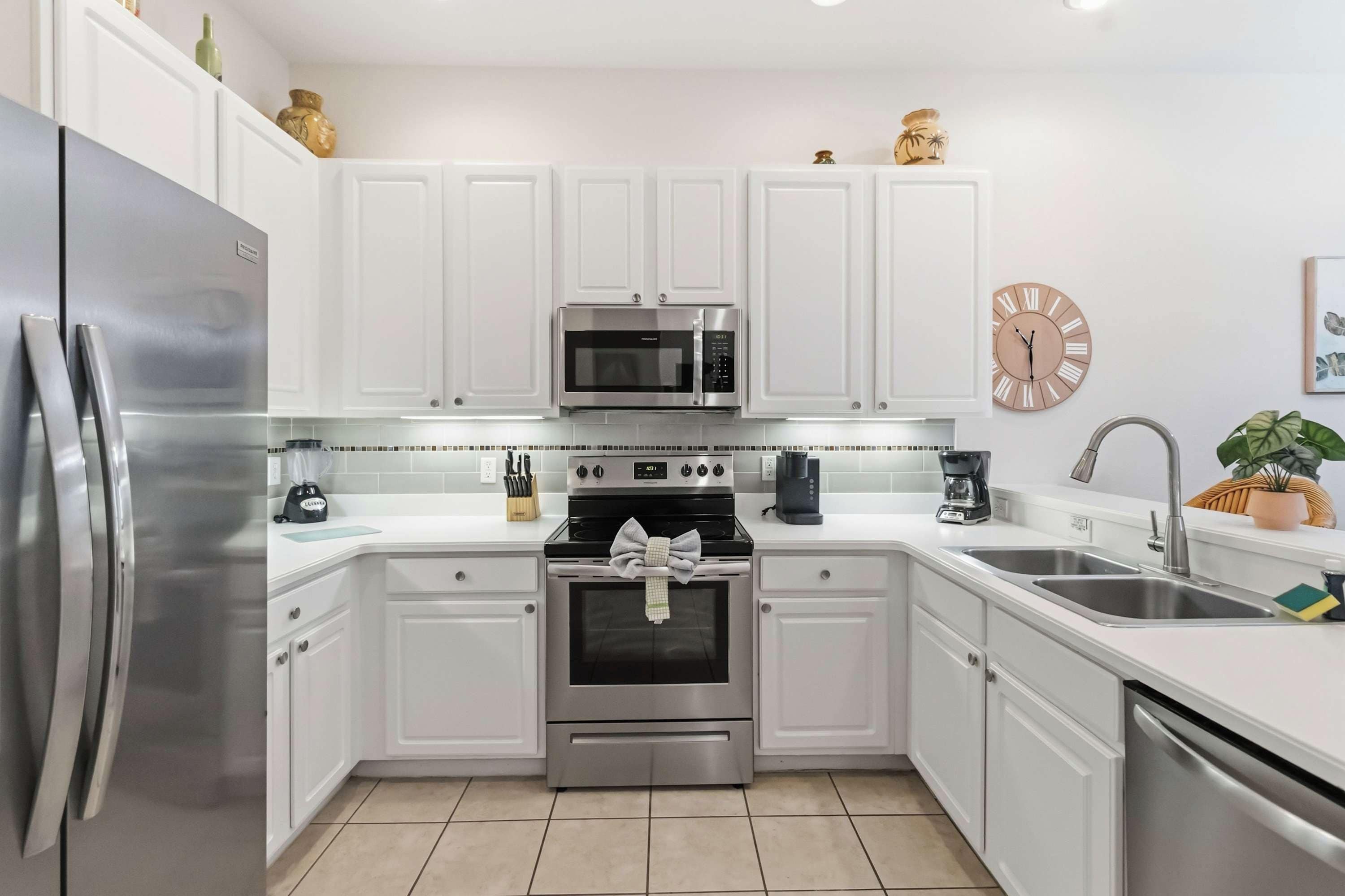 A modern kitchen with white cabinets, stainless steel appliances, a microwave, oven, and a sink.