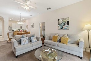 A modern living room with two sofas, a coffee table, and a dining area with wicker furniture.