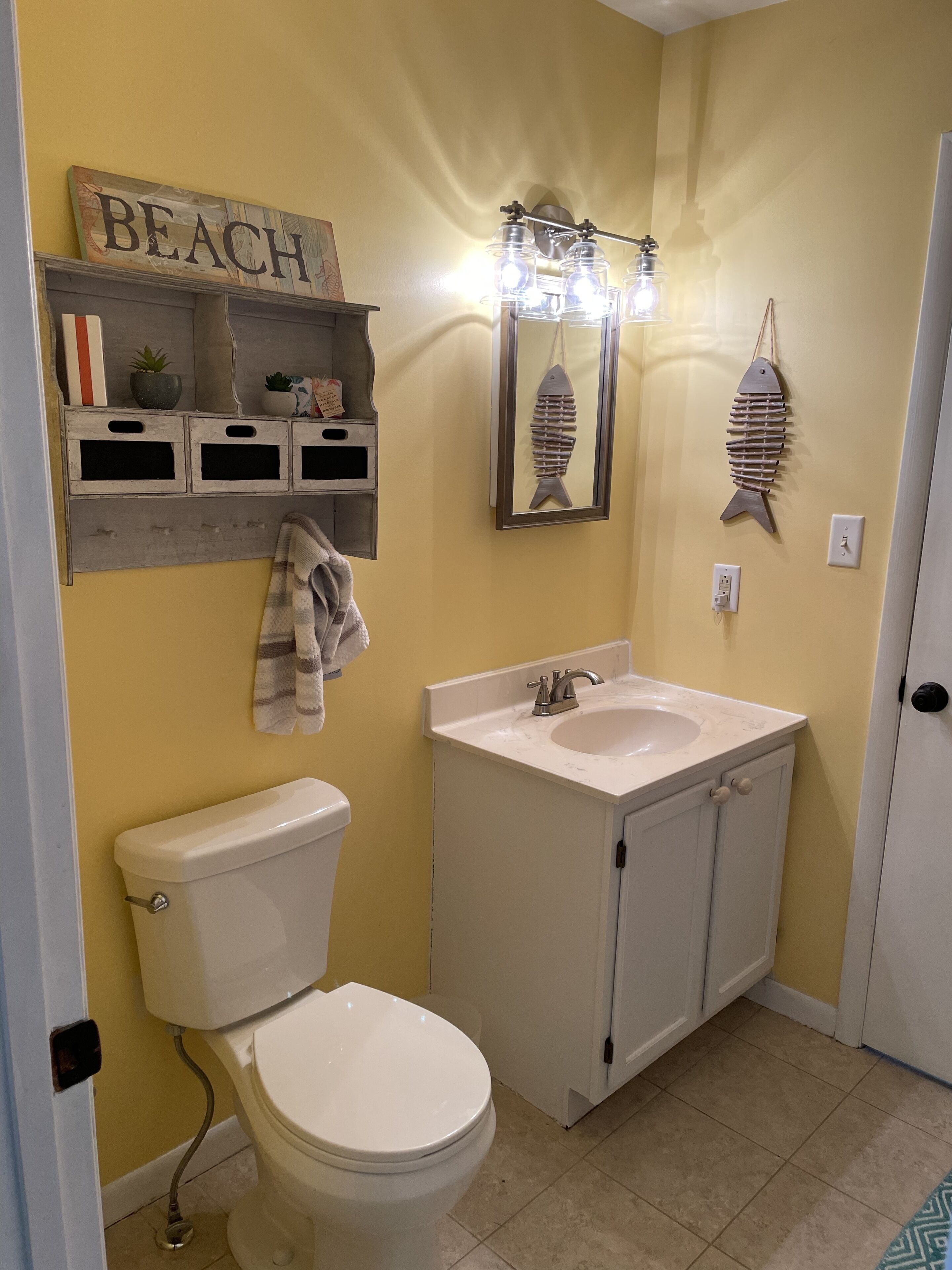 Une salle de bain équipée de toilettes, d’un lavabo et d’une étagère où sont disposés des objets décoratifs.