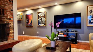 Un salon moderne avec un mur en briques, un téléviseur à écran plat, un pouf en cuir, une table basse agrémentée d’une plante et des affiches de films accrochées au mur.