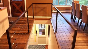 Un escalier en bois avec une barrière en verre, un coin repas avec des chaises et un tableau accroché au mur.