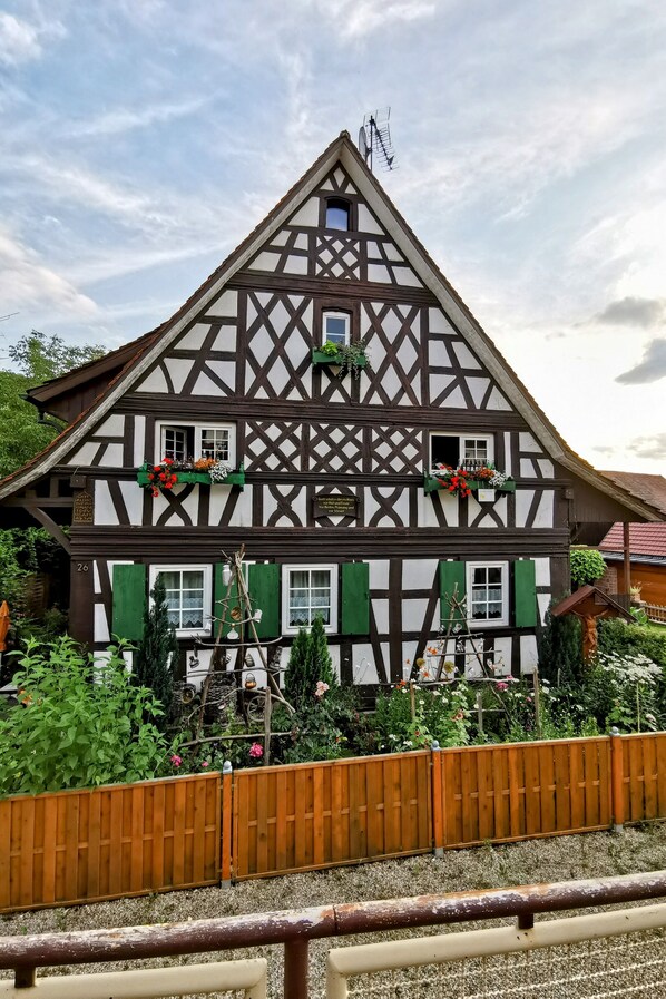 A traditional half-timbered house with a sloped roof, multiple windows, and a wooden fence in the foreground.