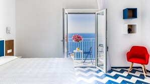A hotel room with a bed, a red chair, a balcony with a view of the sea, and a small table with flowers. - La Vigna di Bacco (Furore)