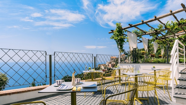 An outdoor terrace with checkered flooring, yellow metal chairs, and tables set for dining. - La Vigna di Bacco (Furore)