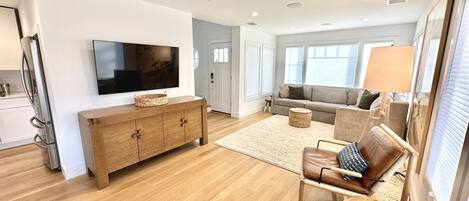 A modern living room with a flat-screen TV, wooden furniture, a sofa, and a dining area with a table and chairs.
