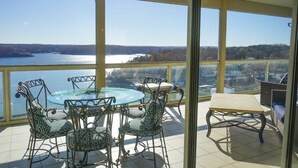 Un balcon avec une table et des chaises en verre, donnant sur un lac et un paysage lointain.