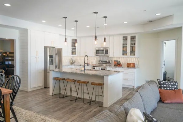 A modern kitchen with white cabinetry, a central island with bar stools, stainless steel appliances, and pendant lighting.